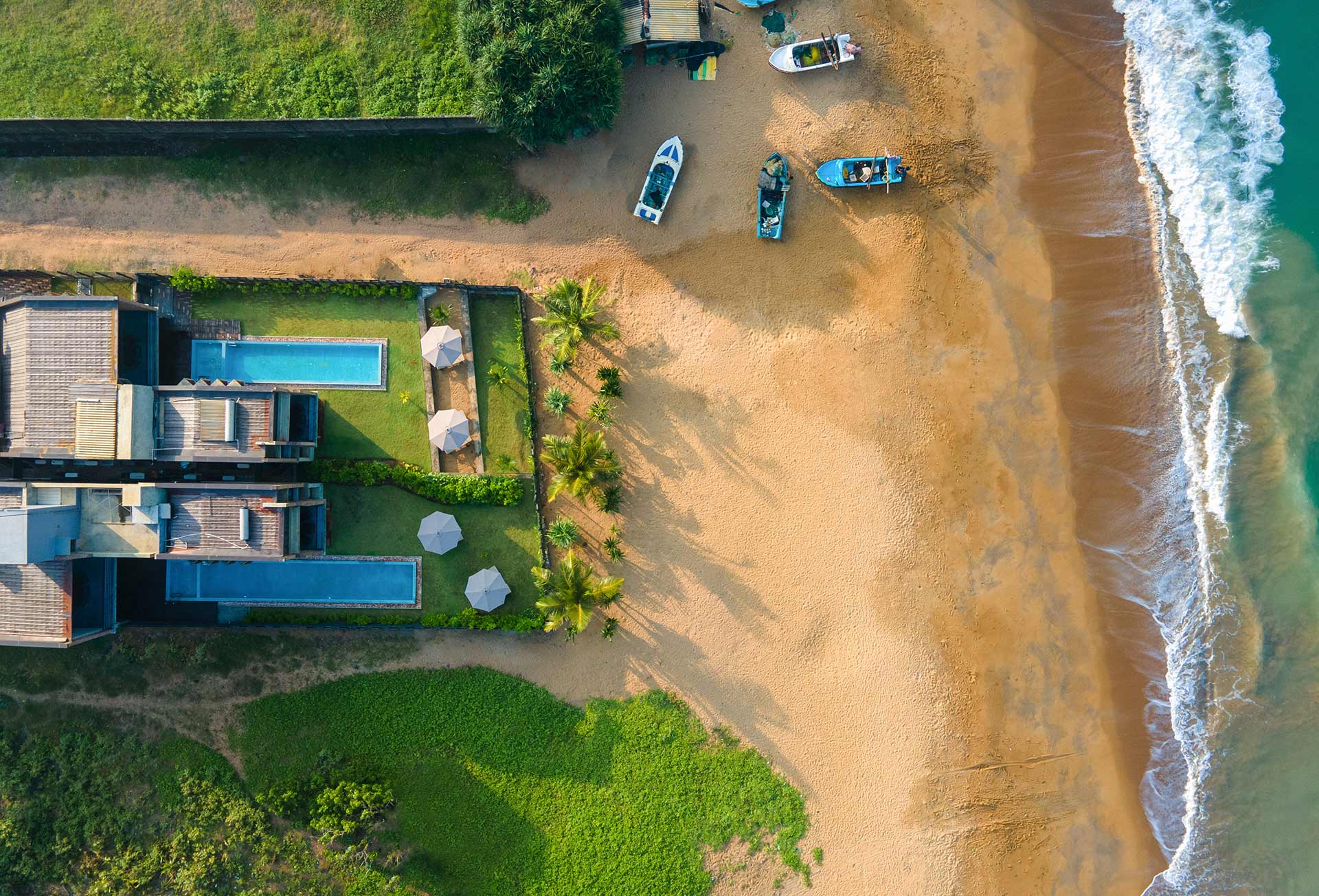 An aerial view of Inidi Leisure Luxury Beach Villa in Wadduwa Sri Lanka, showcasing the beach and a few anchored boats.