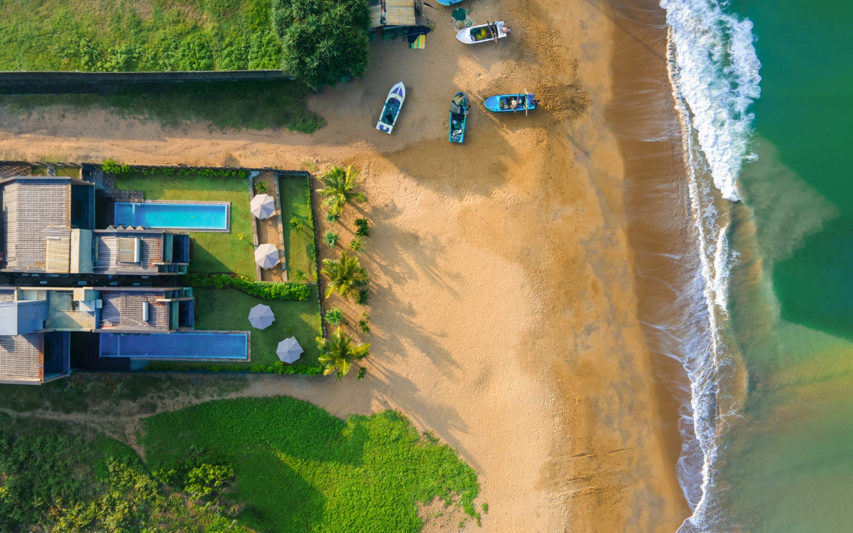 An aerial view of Inidi Leisure Luxury Beach Villa in Wadduwa Sri Lanka, showcasing the beach and a few anchored boats.