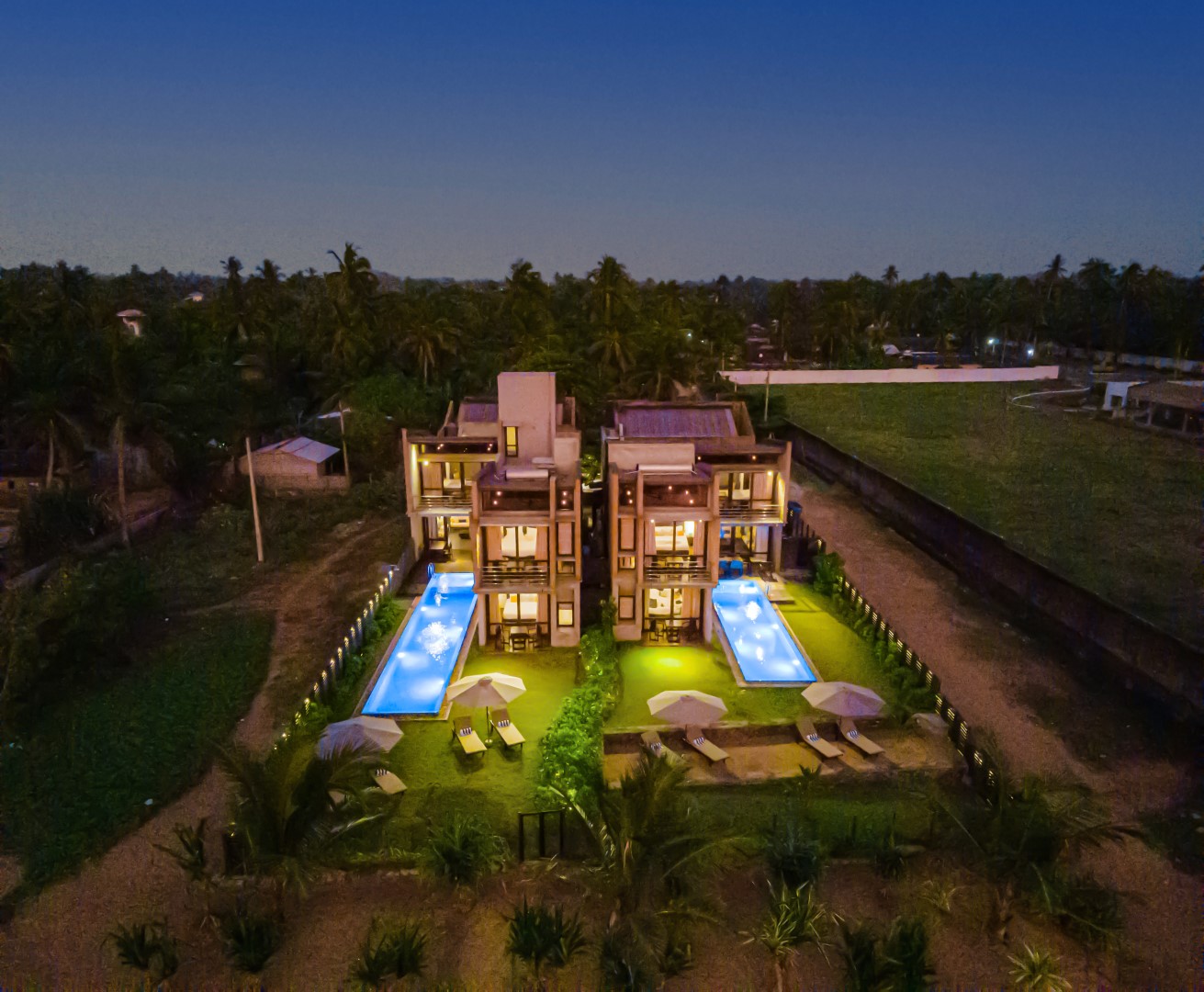 An Aerial view of Inidi Leisure villas,showcasing the neighborhood and lavish coconut plantations. evening view